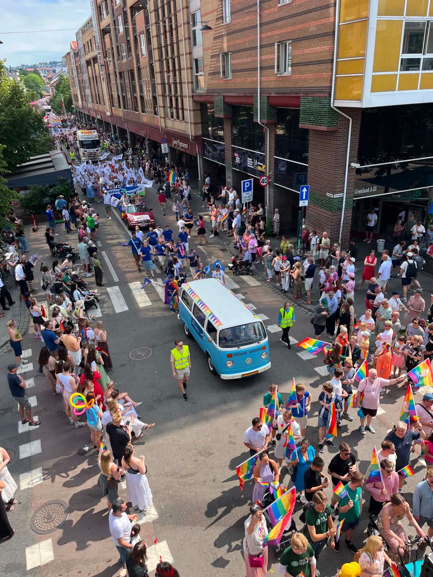 Turkis VW-buss pyntet med regnbuevimpler ruller gjennom Oslo Pride-paraden på Grønland, omringet av folkemengde med regnbueflagg