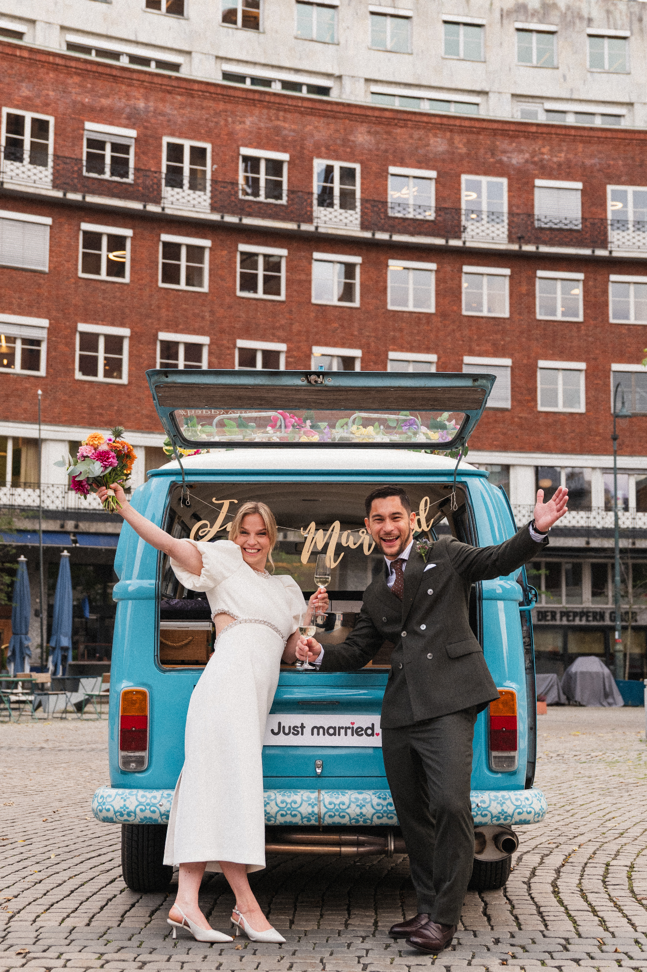 Brudepar feirer bak en blå vintage VW-buss med Just Married-skilt