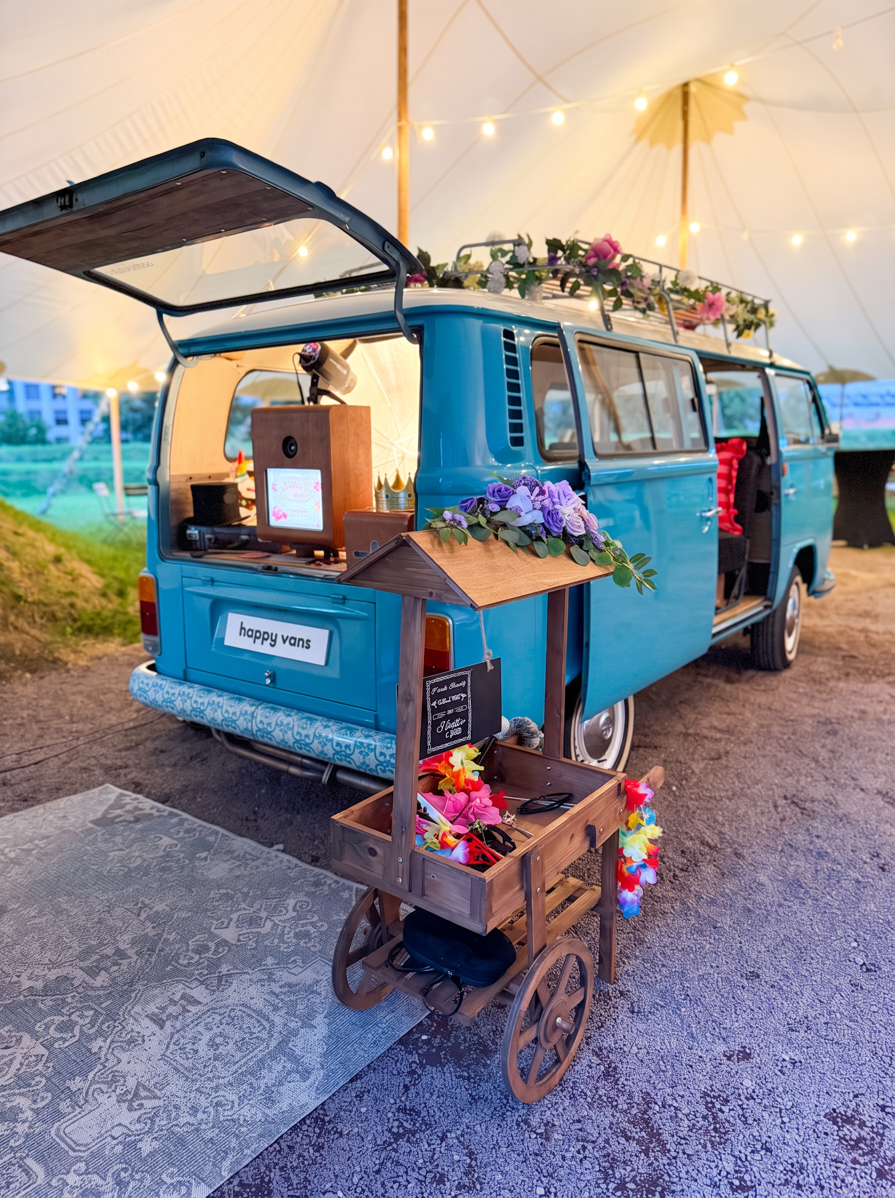 HappySmiles photobooth i bakluken på lyseblå VW-buss med rekvisittvogn i tre og blomsterpynt, inne i teltet på Høymagasinet