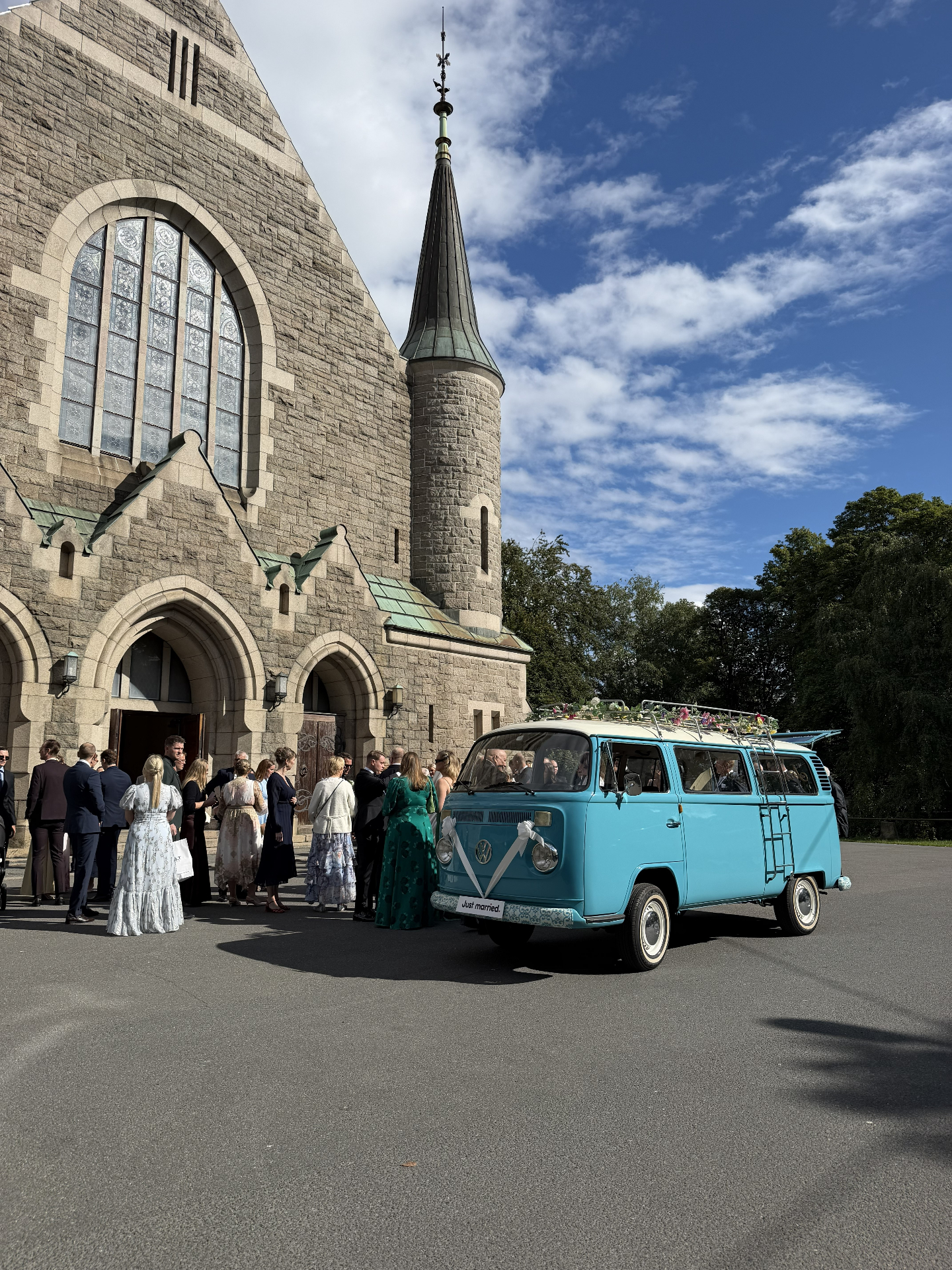 Den turkise VW-bussen står pyntet med blomster utenfor Fagerborg kirke mens bryllupsgjestene samler seg