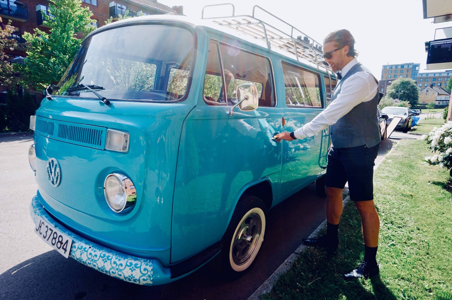 Sjåfør i vest og sløyfe åpner døra på en blå vintage VW-buss