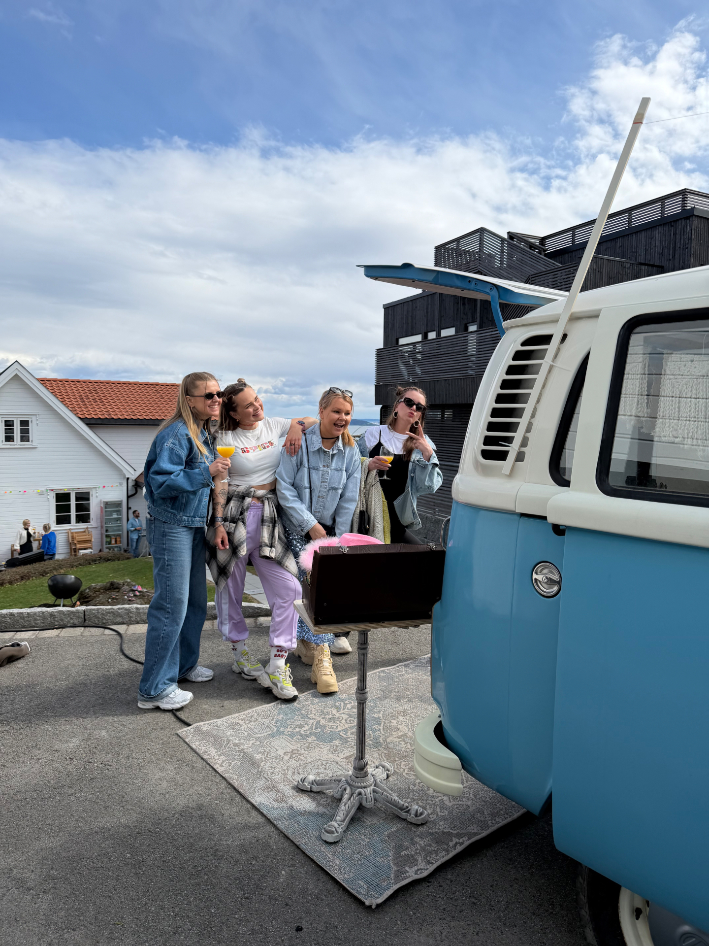 Fire venninner i denimjakker og 90-tallsantrekk poserer bak VW-bussen med drinker i hånden