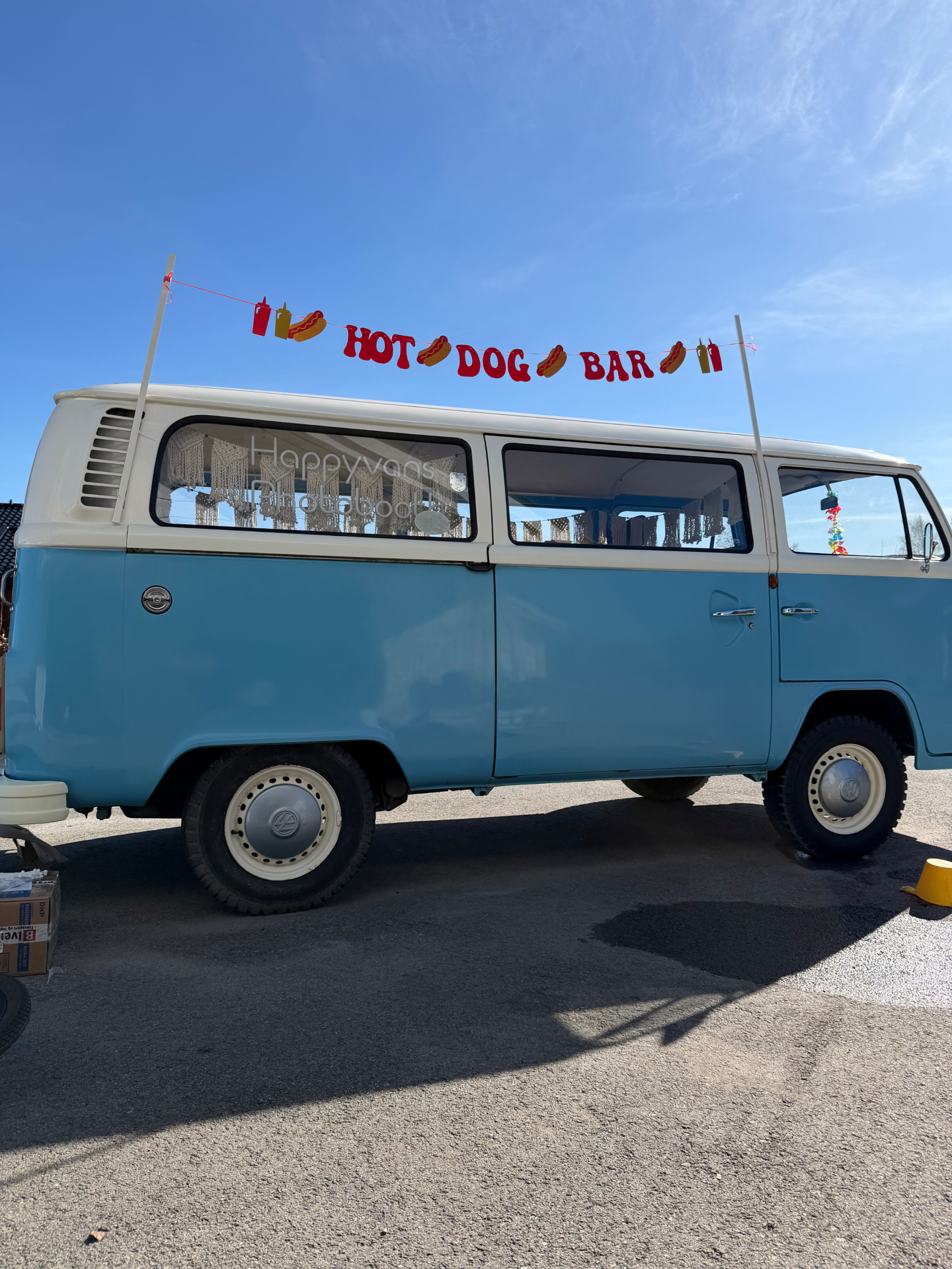 Lyseblå VW-buss med Hot Dog Bar-banner på taket og gjester som mingler foran bussen