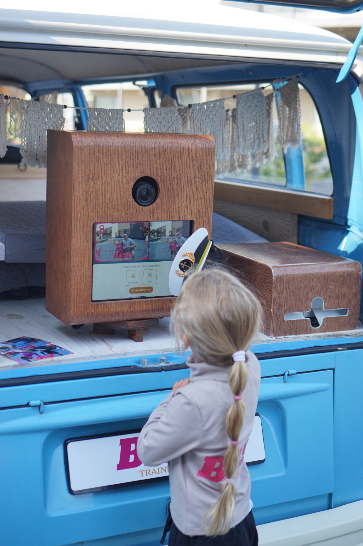 Jente med lang blond flette står foran HappySmiles photobooth i VW-bussen og velger på skjermen