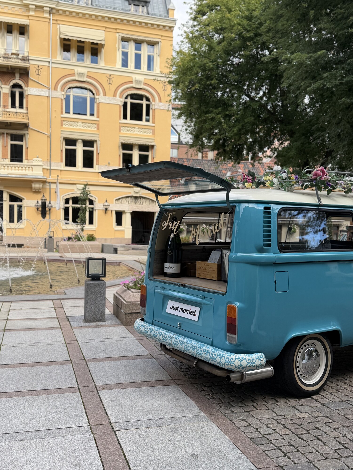 Bakluken på VW-bussen er åpen og viser en stor champagneflaske og Just Married-skilt på Bankplassen